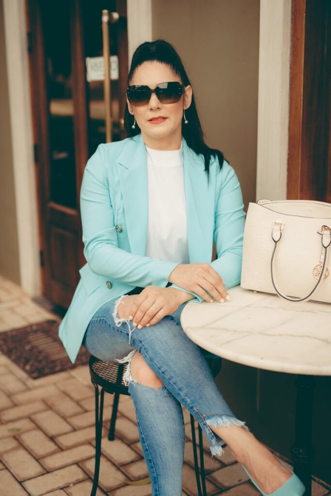 Woman sitting at cafe in blue jacket and jeans, exuding urban elegance.